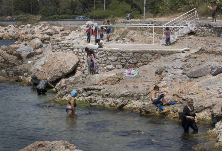 06/01/2017 ATHENS, GREECE (EU) Refugees take a swim to cleanup in the waters of the Gulf of Elefsina, just outside the Skaramagas refugee camp, located 11k west of Athens, where it has become home to 3,000 refugees mostly from Syria, Iraq and Afghanistan, have been settled here to wait out the sometimes years-long relocation process elsewhere in Europe. They live in trailer-like homes 3,200 refugees wait out the sometimes years-long relocation process in caravans, trailer-like homes lined up in rows leading to a common area with a community center, a playground, and offices for non-governmental organizations (NGOs).