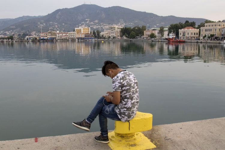 LESVOS, GREECE  06/03/2017: A young migrant checks messages on his phone while sitting by the harbor in Mytilene.  Lesvos is one of the Greek islands most burdened by the refugee crisis; about 8,700 of the 60,000 migrants living in Greek camps are housed here. In recent months, migrants have held protests here over poor living conditions at state-run camps and delays in the processing of their asylum applications, and have sparked clashes with local members of the far-right, whose tolerance of the growing refugee population has worn thin.