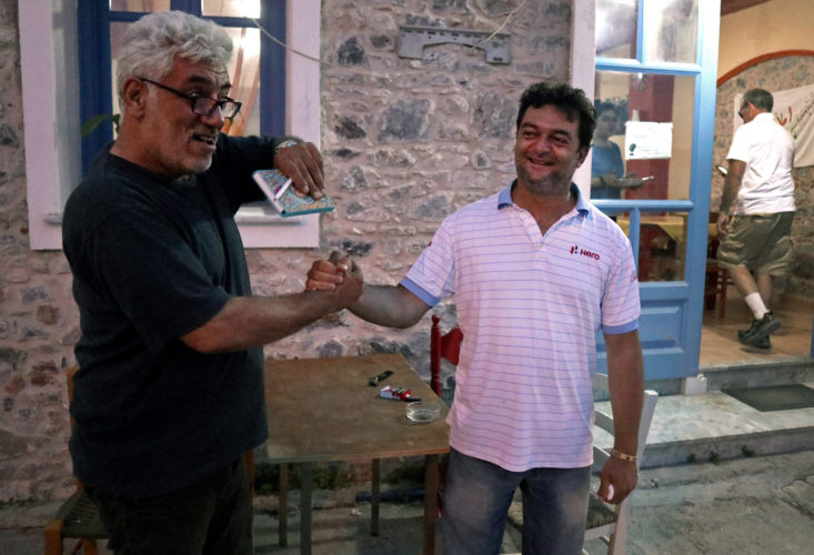 LESVOS, GREECE (EU)  06/03/2017: "Home for All" Restaurant owner Nikos Katsouris, right, welcomes one of the refugee volunteers to his restaurant. He and his wife Katerina have been serving dinner each night to refugees from the nearby camps since 2014, and they have become a gathering point for donations of goods, classes, WiFi, and emotional support, and has become an integral part of Lesvos's humanitarian reputation during the refugee crisis. Since 2014 they have welcomed refugees to their restaurant, giving them a place to eat and feel like they are home for a day. Home is sustained with help from friends, family, and volunteers who purchase food and offer donations to Nikos and Katerina.