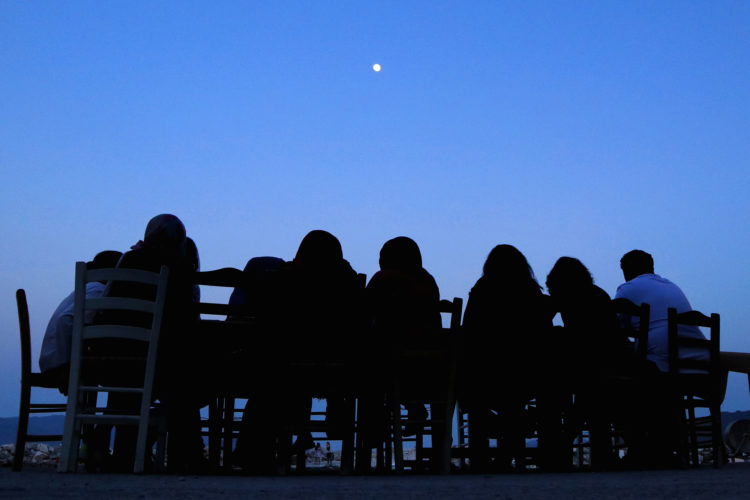 LESVOS, GREECE (EU)  06/03/2017: Refugees and volunteers from the nearby Moria Refugee camp sit down for dinner in the moonlight dinner at "Home for All," the Mytileni restaurant that serves dinner each night to refugees for free.  A harbor-side gathering point for donations of goods and emotional support, 
 Run by restaurant owners Nikos and Katerina Katsouris, Home has become a gathering point for donations of goods and emotional support, for refugees.