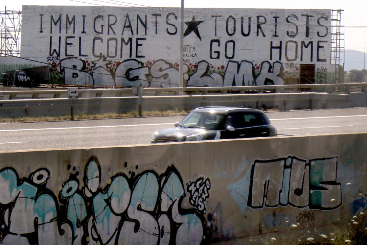 ATHENS, GREECE (EU) 06-10-2017: A pro-immigrant message was spray painted onto a roadside billboard in Athens. As the Syrian refugee crisis continues, nearly 60,000 refugees remain stranded in Greece, according to UNHCR data, and are spread out between three main islands — Lesvos, Chios and Samos — where they face abhorrent conditions, as well as mainland Greece in the cities of Athens and Thessaloniki, where the most environmental damage exists. The influx of nearly 1 million refugees and migrants passing through Greece has had a devastating effect on its environment and economy, particularly during the summers when tourism's high season is in full swing.  The refugee crisis has exacerbated the damage on Greece's already fragile environment, leaving many Greeks worried that tourism — its largest industry — will suffer even more after getting hit hard by the debt crisis that began in 2009.