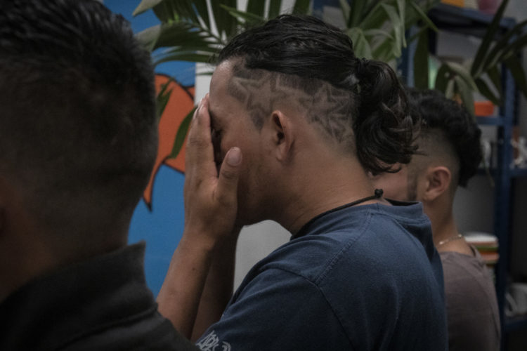 GUADALAJARA, MEXICO   07/13/2017  Mario, a migrant from Honduras, has the stars and stripes from the national Honduran flag shaved into his hair. He is covering his face as he says a silent prayer before dinner in the FM4 Paso Libre shelter in Guadalajara, and now he's preparing to leave FM4 to continue on the journey to the U.S. border.  After leaving FM4 at night, the men walked along the railroad tracks to a position where they can jump on board La Bestia, the moving freight train known as The Beast.