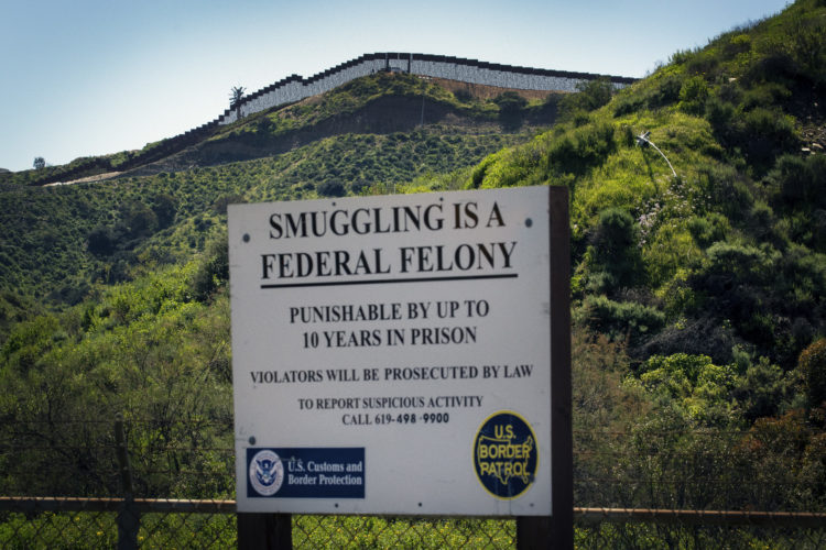 SAN YSIDRO, CA  03/12/2019: A warning sign is posted in International Park in San Ysidro warning that smuggling is a federal offense, as the border wall between Tijuana, Mexico and San Ysidro can be seen in the distance. The U.S.-Mexico border is 1,933 miles long, stretching from the Pacific Ocean to the Gulf of Mexico, roughly 700 of those miles have fencing currently in place.In July 2019, the Supreme Court gave President Trump a victory in his fight for a wall along the Mexican border by allowing the administration to begin using $2.5 billion in Pentagon money for the constructionIn the run-up to his election victory, Mr Trump promised to build a wall along the border's entire 2,000-mile length.He later clarified that it would only cover half of that - with nature, such as mountains and rivers, helping to take care of the rest. But, since Mr Trump entered the White House, although some of the already existing barriers have been replaced, work on extending the current barrier has only just begun