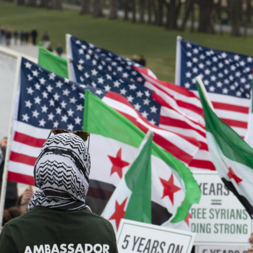 WASHINGTON D.C.  03/20/2016: A woman wearing a head scarf watches the “March for Syrian Freedom” rally in Washington DC marking the 5th Anniversary of the Syrian Revolution. Along with the flags of the U.S. the protesters carried Syrian Revolution flags, which is different that the Syrian national flag.

Five years after it began, Syria’s civil war is among the worst humanitarian crisis of our time. The civil unrest has killed more than 220,000 of its citizens, and it has been estimated that over 11 million people have been forced to leave their homes. Bombings have destroyed cities, human rights violations are widespread, and basic human necessities like food, housing, and medical care are sparse. Roughly half of Syria’s population has fled to either neighboring countries or to Europe, many risking their lives in hopes of finding acceptance and opportunity abroad, while hundreds of thousands remain stranded in refugee camps across the Middle East, Europe, and the Mediterranean region prompting rights groups to accuse the international community of failing Syria.
