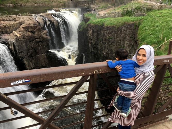 04-19-19 PATERSON, NJ:  Bangladeshi immigrant Tahira Afroz and her 12-month old son Azaan pose for a photo on the walkway over the Great Falls in downtown Paterson, NJ. This was the first time they visited the iconic symbol of the industrial city. The falls of the Passaic River is a prominent waterfall, 77 feet high, on the Passaic River in the city of Paterson in Passaic County, New Jersey, United States. The falls and surrounding area are protected as part of the Paterson Great Falls National Historical Park, administered by the National Park Service.