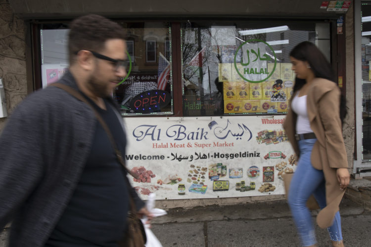 04-19-19 PATERSON, NJ:  Two pedestrians walk past a store's welcome sign, written in English, Turkish and Arabic.