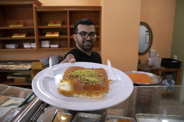 04-19-19 PATERSON, NJ: Mohammad Alsongi serves a fresh plate of Kanefeh at Al Basha Bakery on Main Street in South Paterson. Kanafeh is a popular traditional Levantine dessert made with thin noodle-like pastry, or dough soaked in sweet, sugar-based syrup, and typically layered with cheese, or with other ingredients such as clotted cream or nuts.